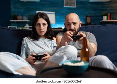 Focused Determined Gamers Playing Soccer Videogame Late At Night Trying To Win Online Competition. Couple Sitting On Sofa, Gaming Video Games Together Using Joystick, Wireless Controller