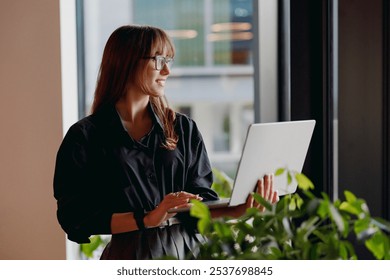 A focused and determined young woman intensely using a laptop in a bright, modern office space adorned with plants - Powered by Shutterstock