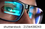 Focused developer coder wears glasses working on computer looking at programming code data cyber security digital tech reflecting in spectacles developing software program, focus on eye close up view.