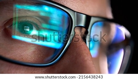 Focused developer coder wears glasses working on computer looking at programming code data cyber security digital tech reflecting in spectacles developing software program, focus on eye close up view.