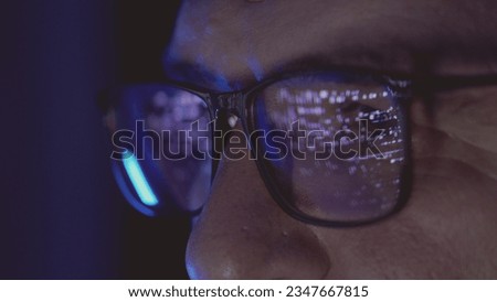 Focused developer coder wears glasses working on computer looking at programming code data cyber security digital tech reflecting in spectacles developing software program, focus on eye close up view.