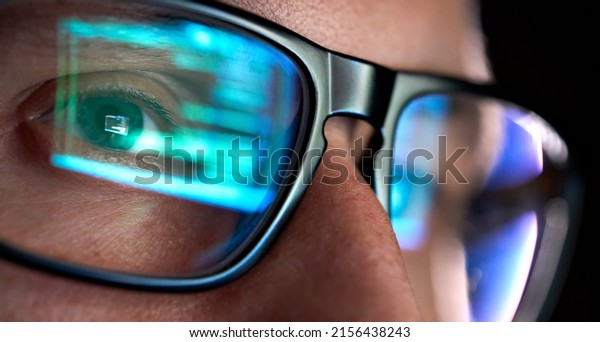 Focused developer coder wears glasses working on\
computer looking at programming code data cyber security digital\
tech reflecting in spectacles developing software program, focus on\
eye close up view.