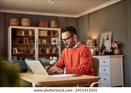 A focused and diligent adult male online content writer typing on his laptop and sitting at a wooden desk in his home office. 商業照片 © 