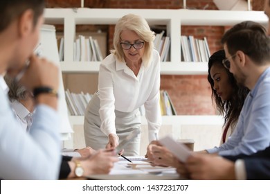 Focused diverse business executive team people with old middle aged boss manager discuss paperwork at group meeting, senior mature female leader presenting financial report work plan at briefing