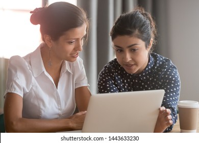 Focused Diverse Ethnicity Female Coworkers Team Brainstorming Pointing On Laptop, Two Serious Indian And Caucasian Business Women Colleagues Share Ideas Sit At Work Desk Looking At Computer In Office