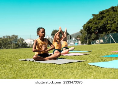 Focused diverse schoolgirls practicing yoga and meditating at stadium on sunny day. School, activity and education, unaltered. - Powered by Shutterstock