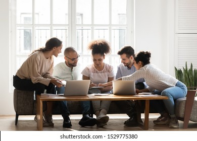 Focused Diverse Students Working On Research Project For College Or University Together At Home, Sitting On Couch, Classmates Friends Discussing Reading Notes, Sharing Ideas, Using Laptops