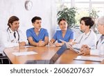 Focused doctors and nurses of different ages gathering in council at table and talking in meeting room