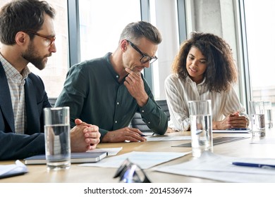 Focused doubtful mature businessman reading contract document thinking considering risks with professional lawyers legal experts executive team analyzing financial report sitting at office table.