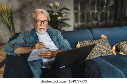 Focused elderly man writing notes in notebook watching webinar or online training using laptop computer, modern senior male with gray hair and beard learning online - Powered by Shutterstock