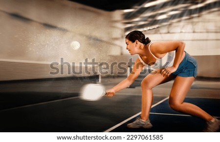 Focused emotional young female pickleball player preparing to perform stroke to return ball on indoor court. Concept of competition emotions..