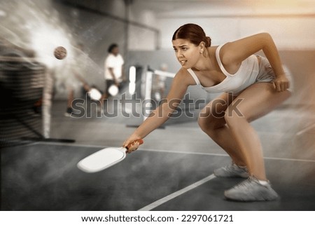 Focused emotional young female pickleball player preparing to perform stroke to return ball on indoor court. Concept of competition emotions..