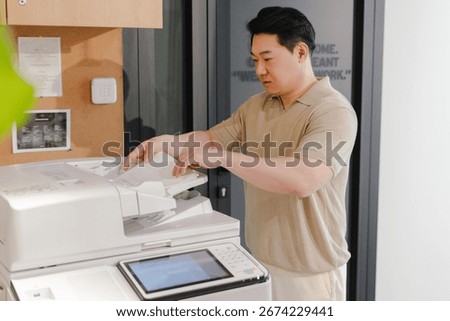 Focused employee using a modern multifunction printer in a contemporary office setting, performing everyday tasks and improving productivity