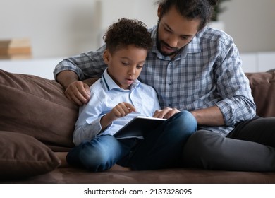 Focused engaged dad helping son to use online learning educational app on tablet computer, sitting on couch at home, watching boy doing school homework, working on electronic task - Powered by Shutterstock