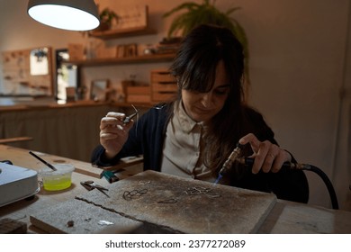 Focused ethnic female goldsmith with dark hair soldering jewellery with torch while working in studio - Powered by Shutterstock