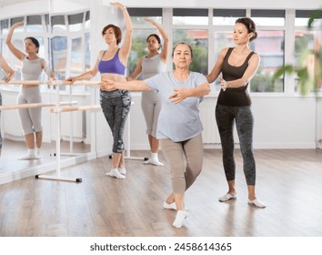 Focused female ballet choreographer patiently instructing senior woman in basic ballet techniques at group dance class for amateurs in spacious light-filled studio.. - Powered by Shutterstock