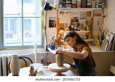 Focused female ceramist shaping potter vase in studio creating ceramics. Artwork for entertainment or small business: artistic workshop owner woman busy with pottery production in creative space room - Powered by Shutterstock