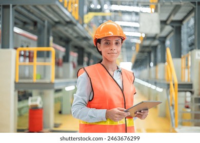 A focused female engineer in an orange safety jacket and helmet is holding a tablet in a train maintenance hall. - Powered by Shutterstock