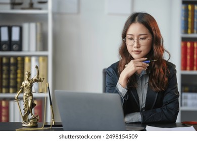 Focused female lawyer works on a legal case in her office, surrounded by law books and documents, using a laptop to research and analyze - Powered by Shutterstock