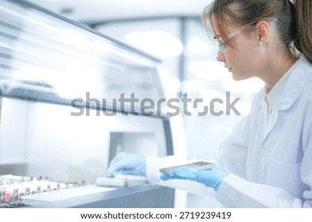 Focused female scientist loading a sample rack into an automated machine in a sterile clinical laboratory. Professional researcher working on pathology diagnosis for medical healthcare projects.