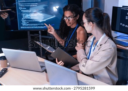 Focused female software engineer discuss project script via laptop. Diverse tech startup coder woman use tablet to check computer program code and web database development in office meeting