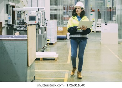 Focused Female Technician With Open Laptop At Printing House. Concentrated Factory Employee Walking At Workplace. Print Manufacturing Concept