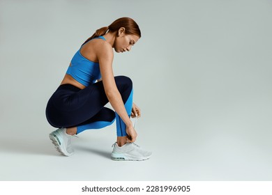 Focused fitness woman tied her shoelaces before training on studio background. High quality photo