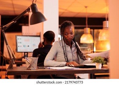 Focused Freelancer Looking At Business Charts On Documents, Analyzing Research Information On Paperwork To Create Research Project. Working With Papers And Computer In Office With Big Windows.