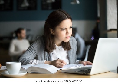 Focused Girl Concerned About Difficult Online Assignment Looking At Laptop Screen Studying Working In Cafe, Millennial Student Thinking Of Problem Solution Reading Hard Task On Computer Making Notes