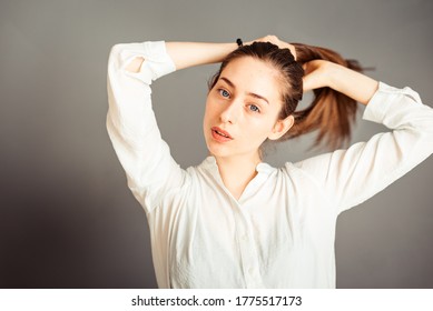 Focused girl does hairstyle, ponytail on a gray background, close-up. Without makeup, without retouching.