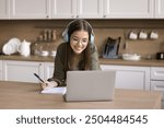 Focused girl in headphones take notes, watch on-line course using laptop, studying with tutor, improve foreign language knowledge, prepare for exams, take part in educational webinar. Education, tech