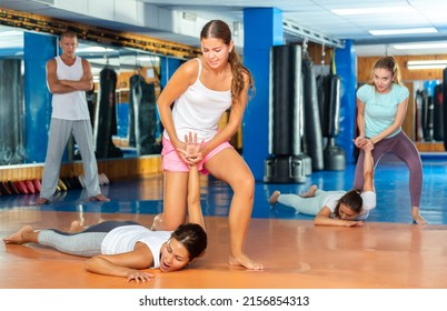 Focused girl learning effective self defence techniques in sparring with man, practicing painful pronating wristlock on opponent lying face down on floor in gym