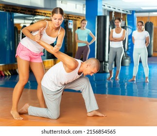 Focused girl learning effective self defence techniques in sparring with man, practicing painful wristlock on opponent standing on knee in gym