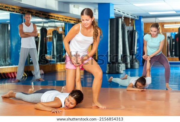 Focused girl learning effective self
defence techniques in sparring with man, practicing painful
pronating wristlock on opponent lying face down on floor in
gym