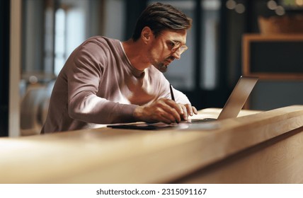 Focused graphic designer drawing on a graphics tablet in a cafe. Business man working on a design with a laptop. Male design professional working remotely. - Powered by Shutterstock