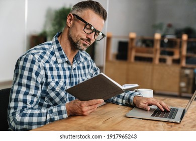 Focused grey man reading while working with laptop in office - Shutterstock ID 1917965243
