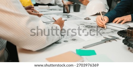 A focused group of engineers collaborates on technical drawings, utilizing tools and notebooks on a modern workspace table, fostering creativity and innovation. SACTR