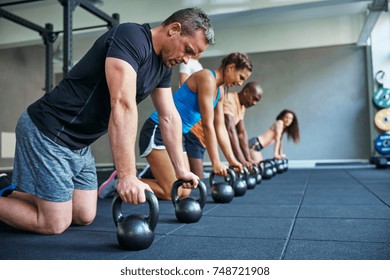 Focused Group Of Fit People Working Out Together On The Floor With Weights During A Health Club Class