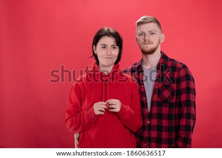 Focused guy looking at camera, grimace girl looking away. casual dressed attractive couple posing on red backdrop with different emotions copy space. relationship problems, Sexual disharmony concept
