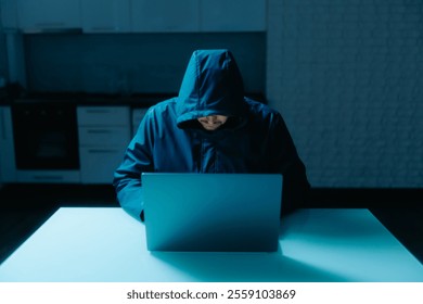 Focused hacker in a dark room, wearing a hooded sweatshirt, working on a laptop at home. A dangerous and mysterious scene depicting modern cybersecurity threats. - Powered by Shutterstock