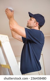 Focused handyman installing smoke detector with screwdriver on the ceiling