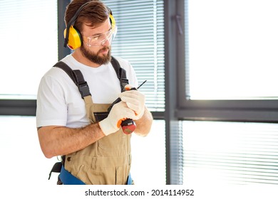 Focused Handyman In Safety Glasses And Overall, Hold Electric Power Tool In Hands, Going To Repair House, Looking Serious. Side View