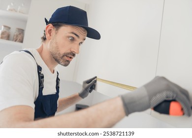 Focused handyman using a measuring tape for home renovation with precision and skill in a modern apartment space - Powered by Shutterstock