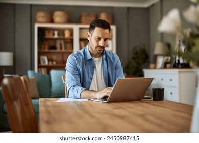 A focused and hardworking young adult male freelancer working on his project on a laptop in a home office environment. - Powered by Shutterstock