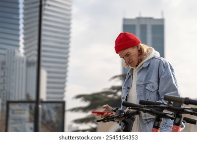 Focused hipster guy using mobile application in smartphone to rent electric scooter for driving in city, town. Urban mobility. Innovative ecological environmental friendly green transport  - Powered by Shutterstock