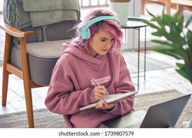 Focused hipster teen girl school college student pink hair wear headphones write notes watching webinar online video conference calling on laptop computer sit on floor working learning online at home. - Shutterstock ID 1739807579