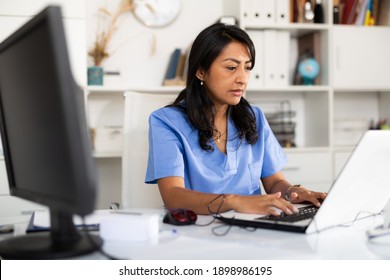 Focused Hispanic Female Doctor Working With Laptop In Clinic Office. Modern Medicine And Healthcare Concept