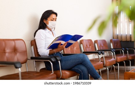 Focused Hispanic Female Entrepreneur In Disposable Medical Mask Reading Attentively Documents In Office Hall While Waiting For Meeting With Investors. Precautions During Coronavirus Pandemic