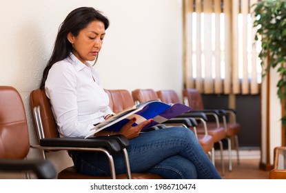 Focused Hispanic Female Entrepreneur Sitting In Office Hall Waiting For Meeting With Investors Or Business Partner, Reading Attentively Documents.