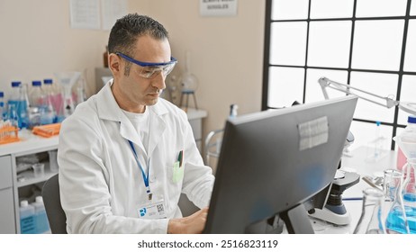 A focused hispanic male scientist in a lab coat studies data on a computer in a modern laboratory setting. - Powered by Shutterstock